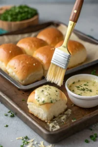 Garlic butter being brushed over the top of slider buns